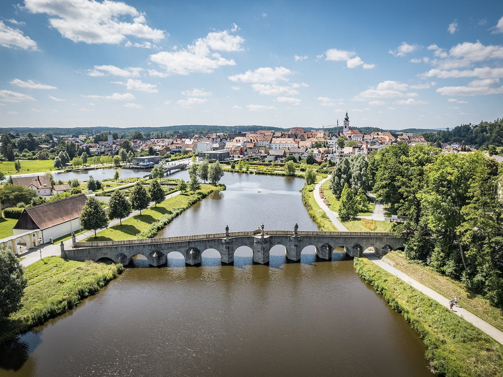 Tirschenreuth Blick auf eine Brücke über einen Fluss, umgeben von Bäumen und einer Stadtlandschaft.